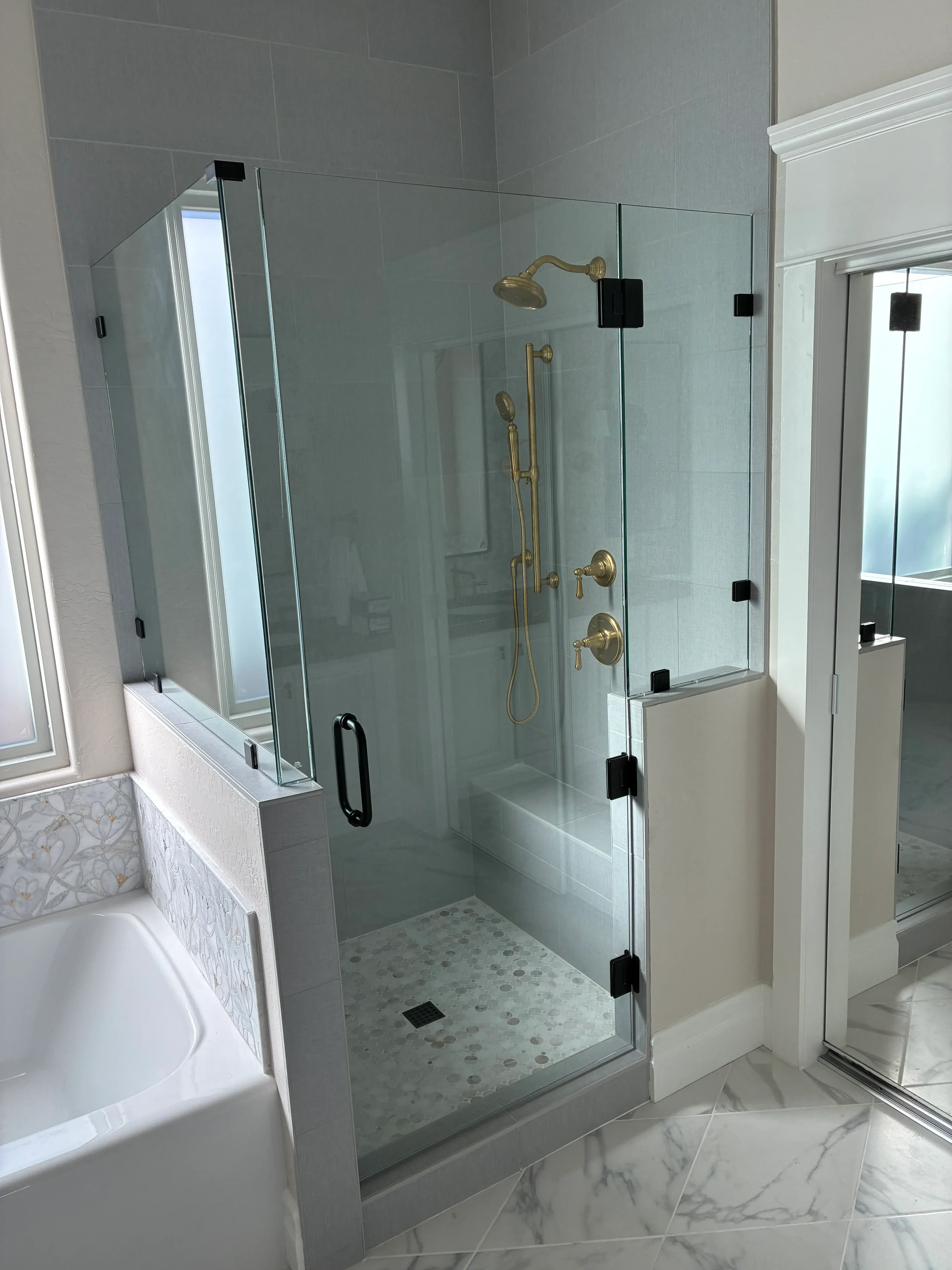 Frameless glass shower enclosure with brushed brass fixtures and marble tile surround