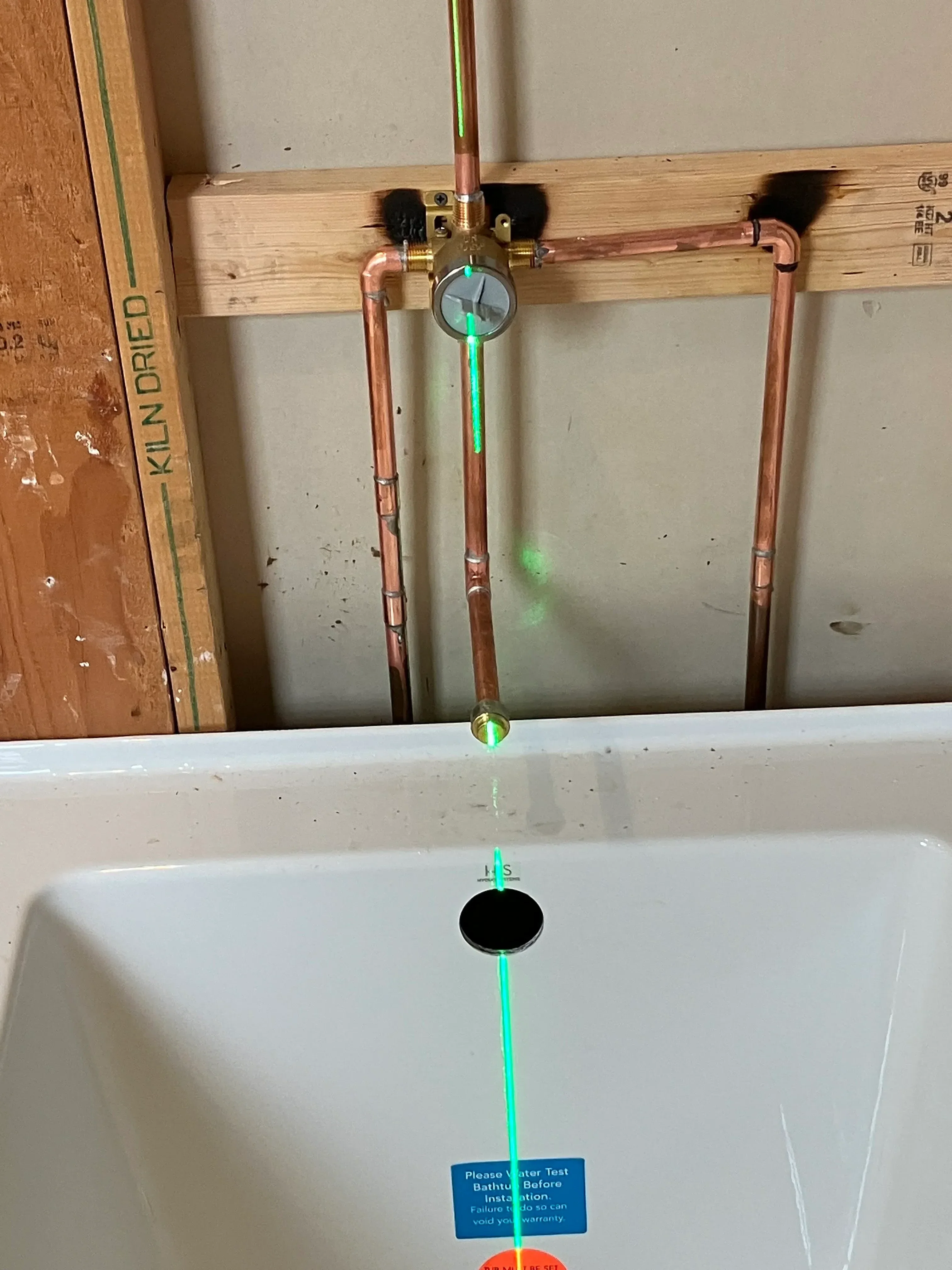 Copper refrigerant lines with gauge, green tubing, and pressure test kit on drywall