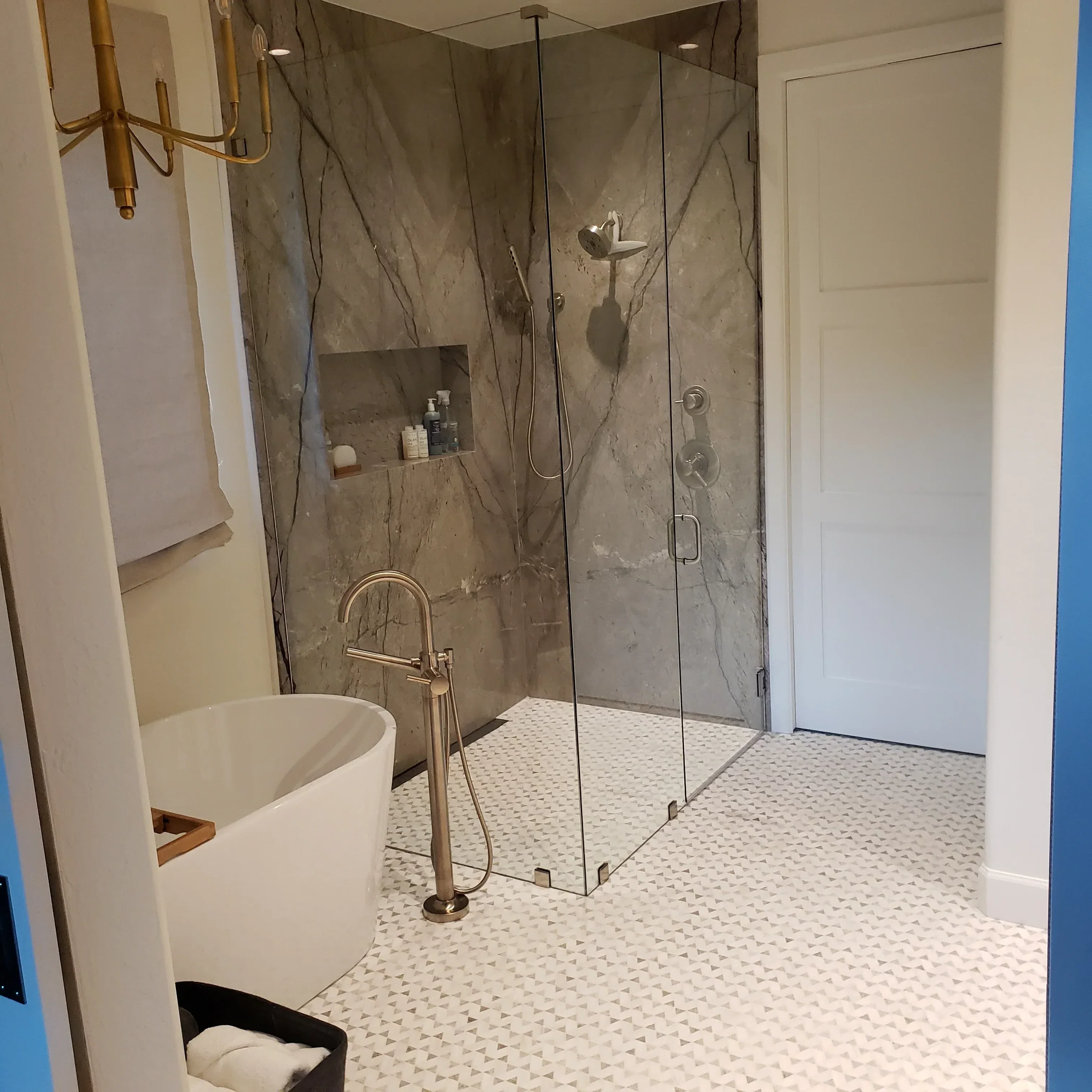Marble tile shower surround with brass fixtures and white textured tile accent wall