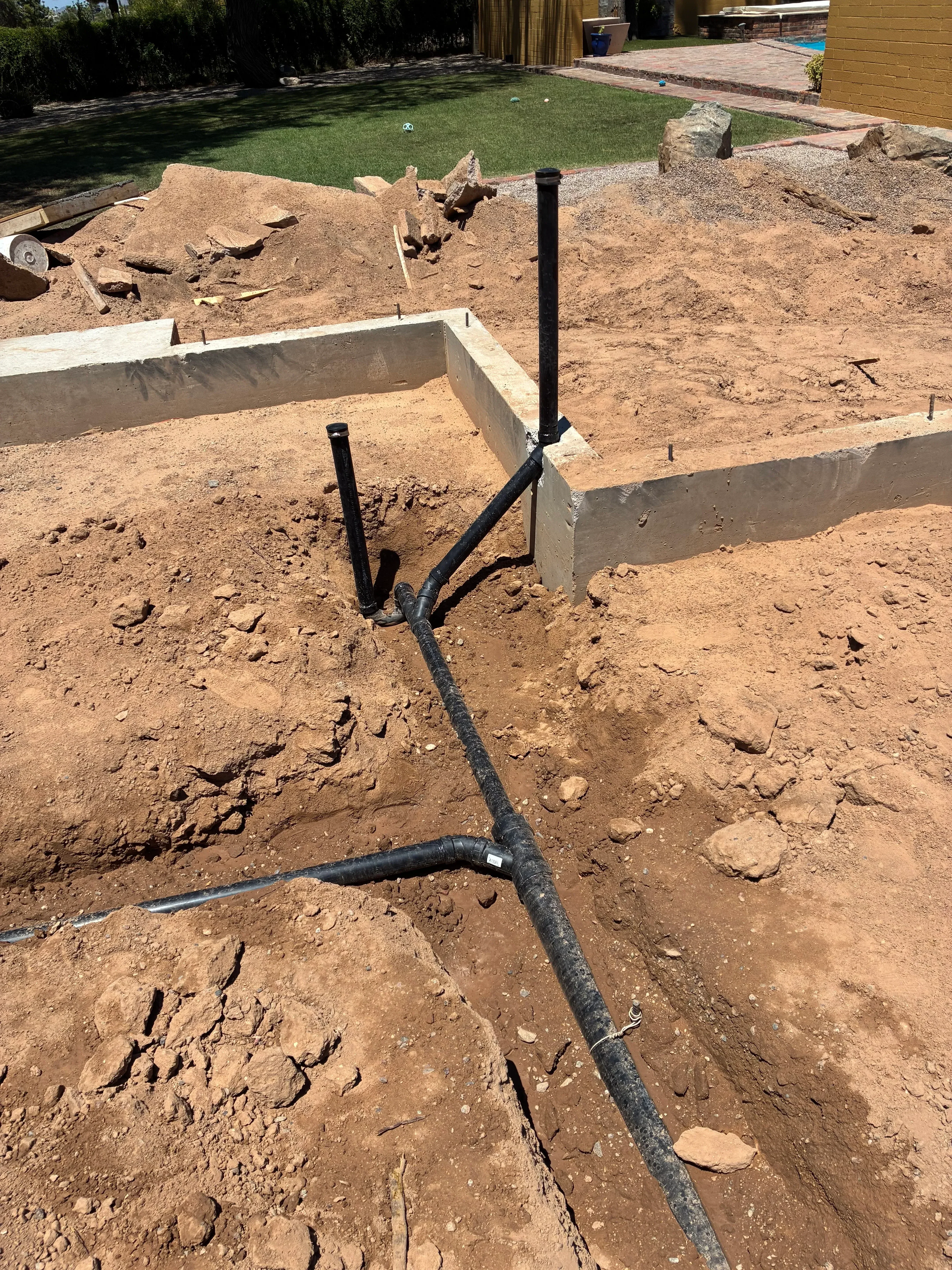 Underground drainage pipe installation with black poly tubing and metal connectors in excavated soil trench
