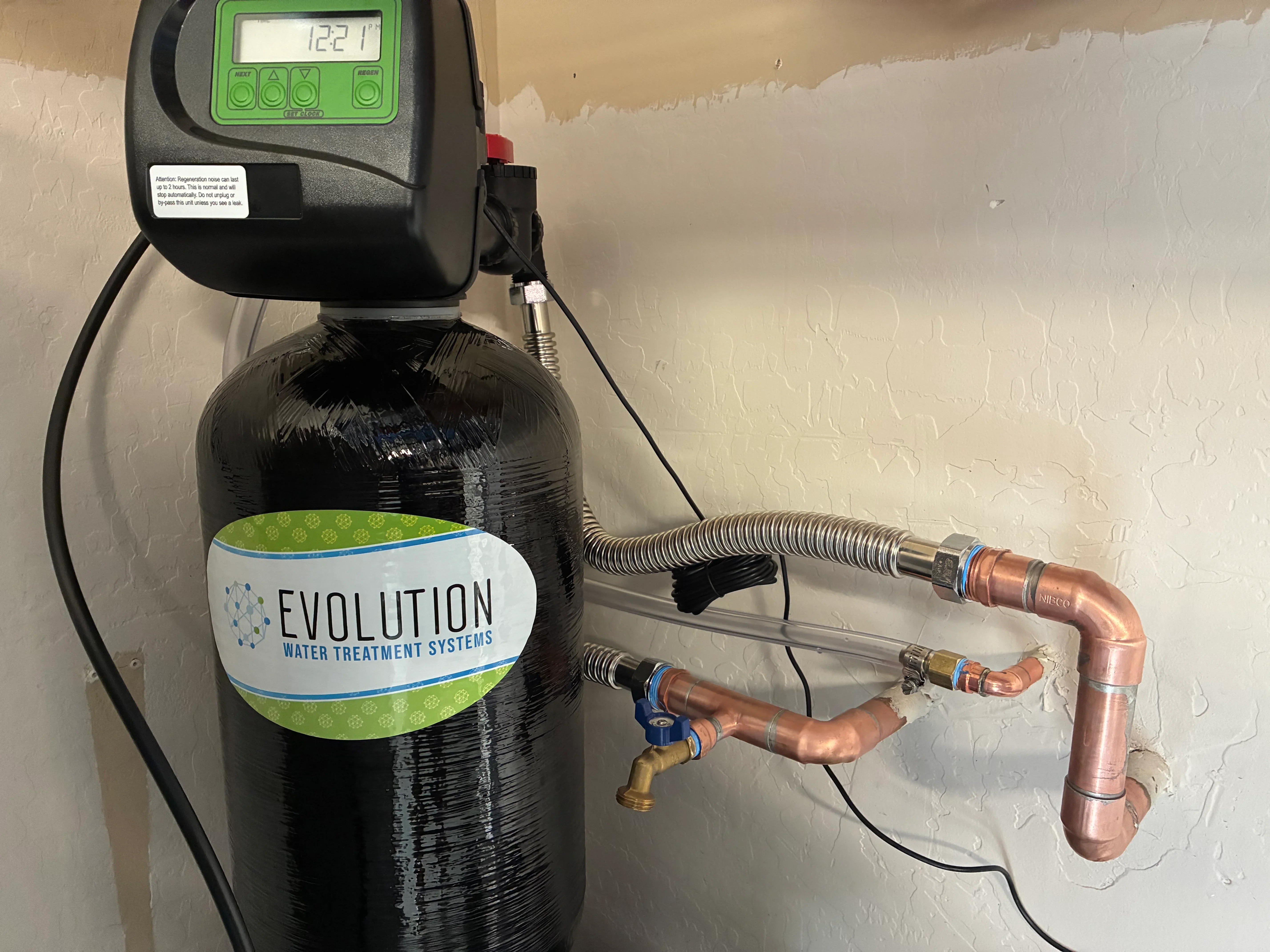 Water softener tank with digital meter, copper piping, and brass valves installed on wall