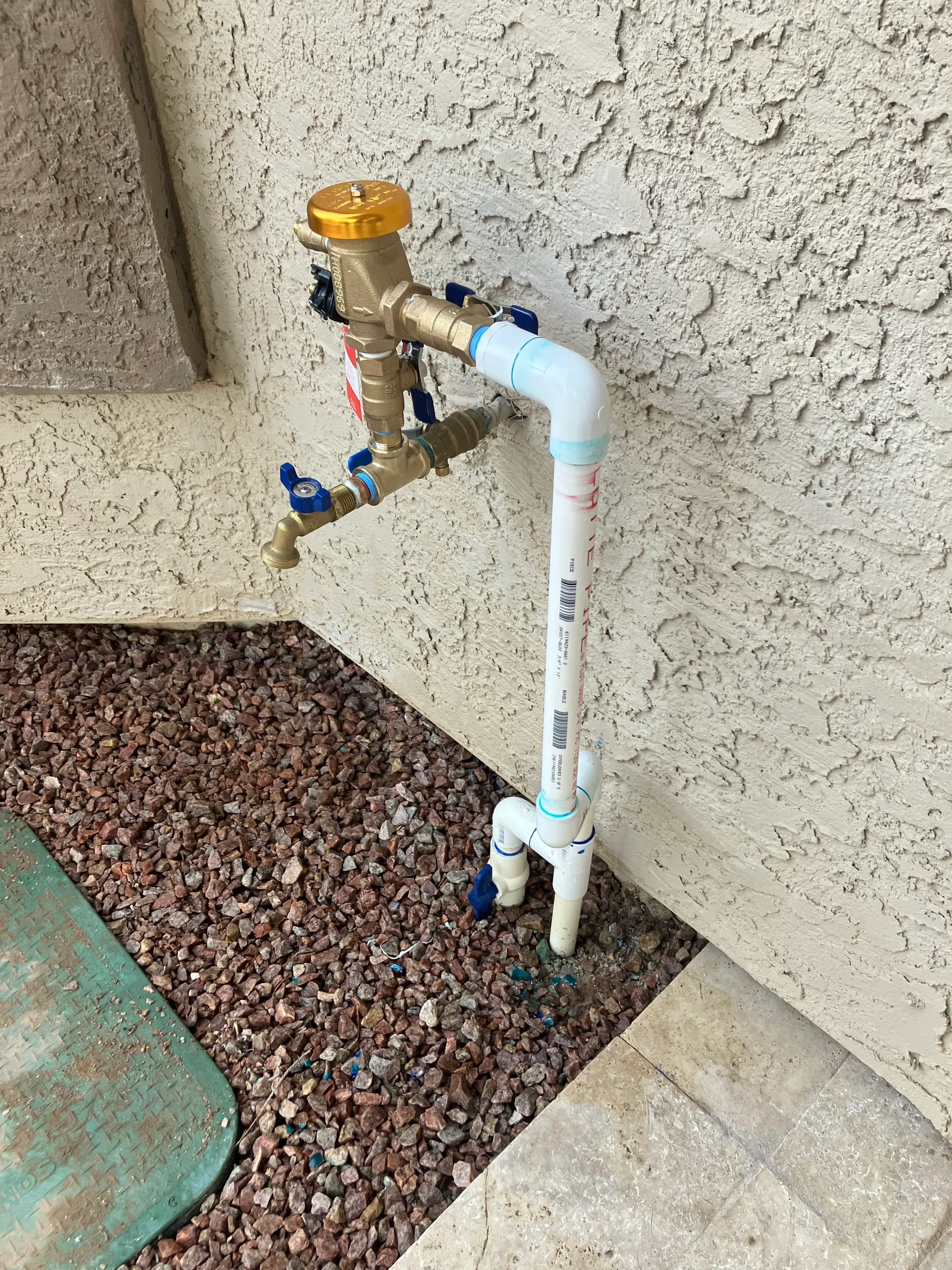 Brass ball valve with blue handles and white PVC piping installed on concrete foundation