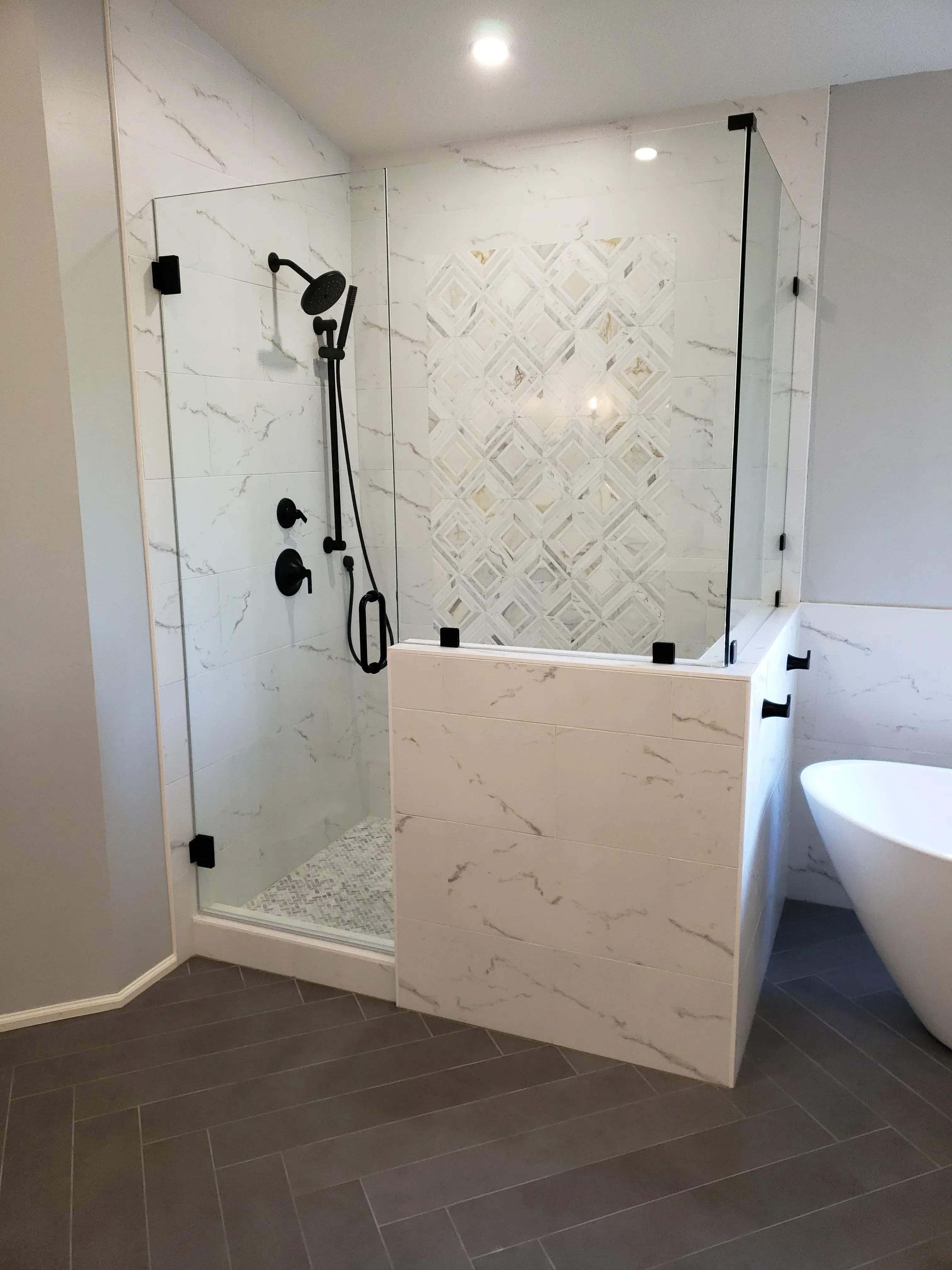 Marble tile shower with geometric accent wall, glass door, and black matte fixtures