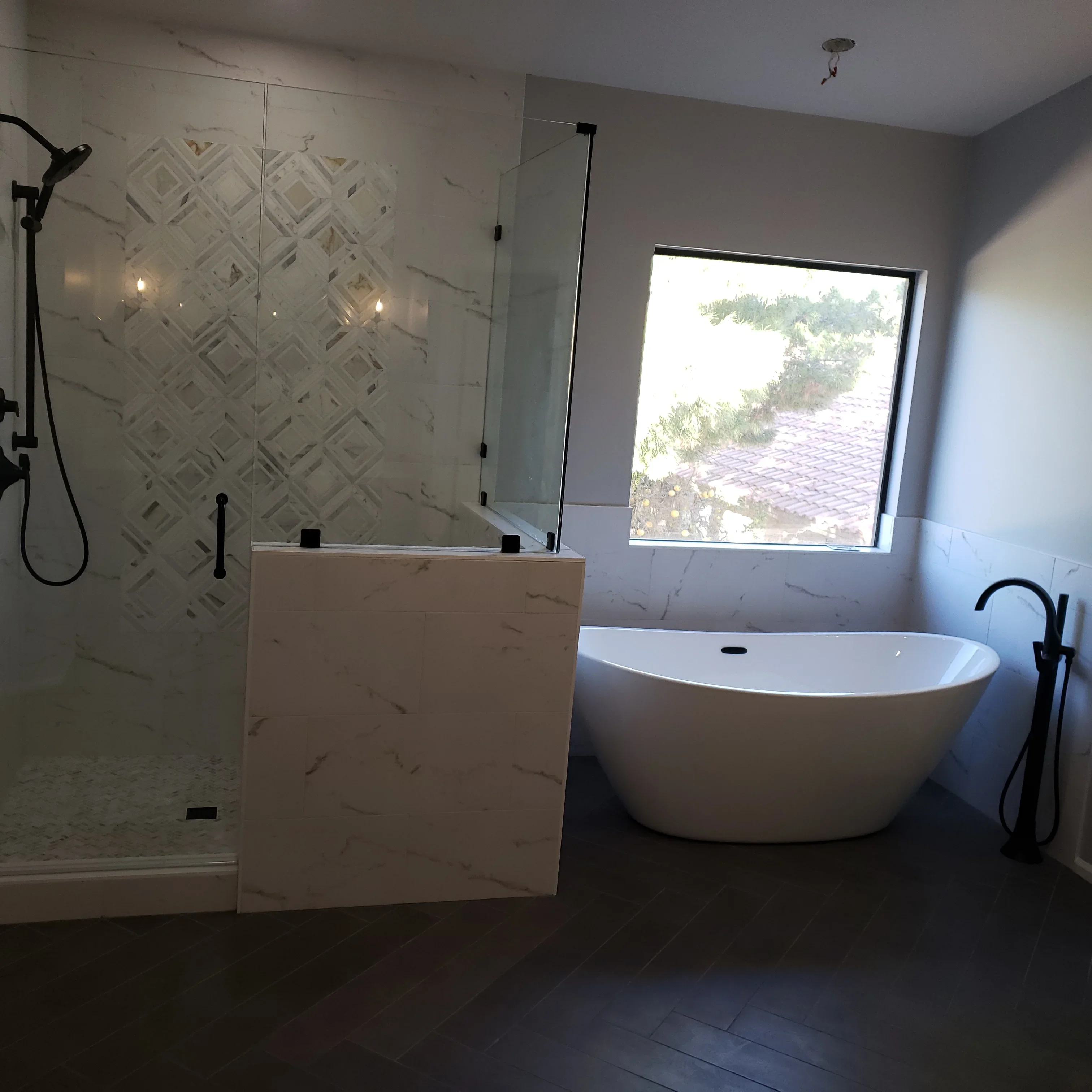Marble tile bathroom with frameless shower, freestanding tub, and black fixtures