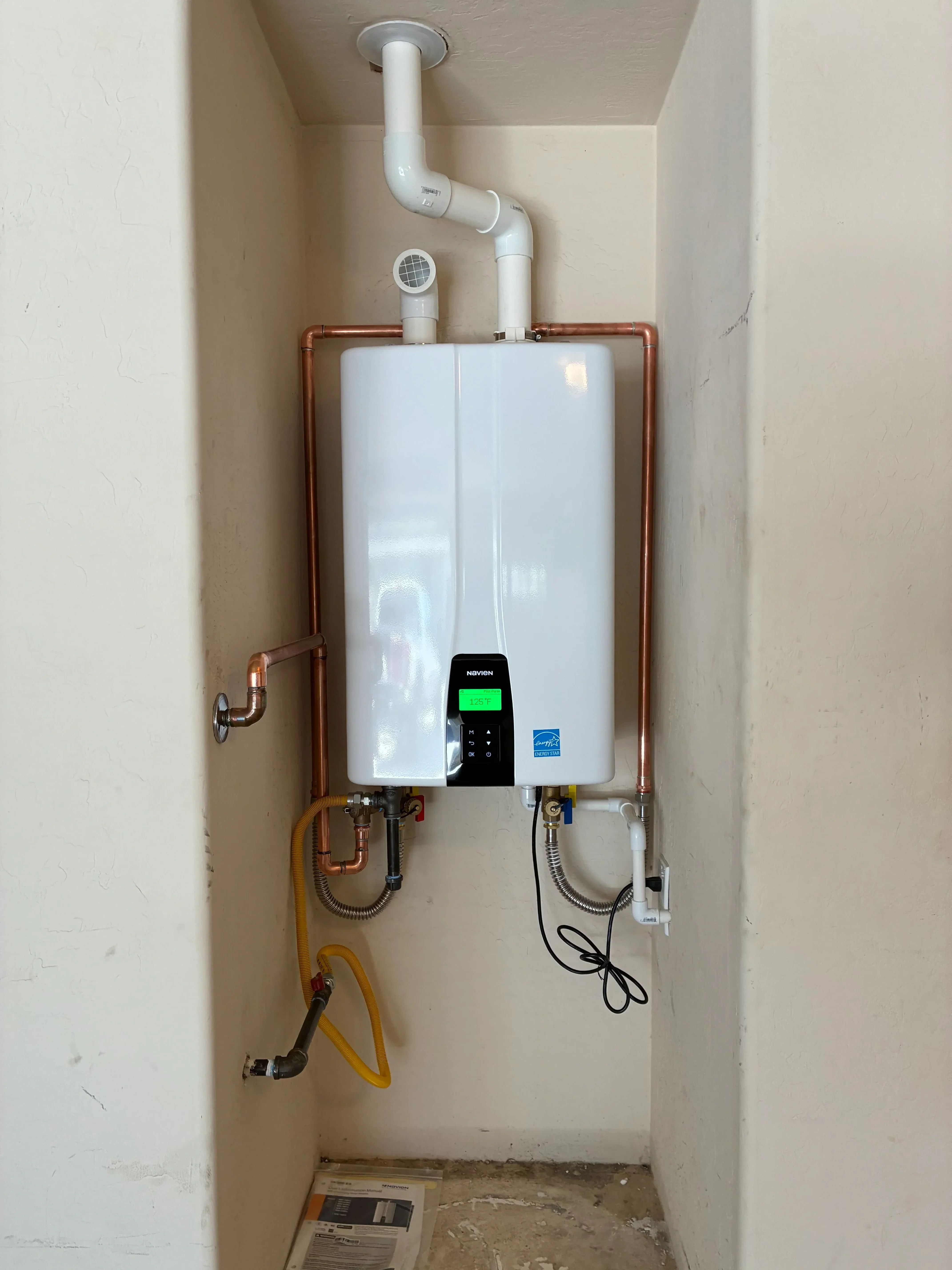 Tankless water heater with copper piping, digital controls, and gas line connections installed in ceiling cavity
