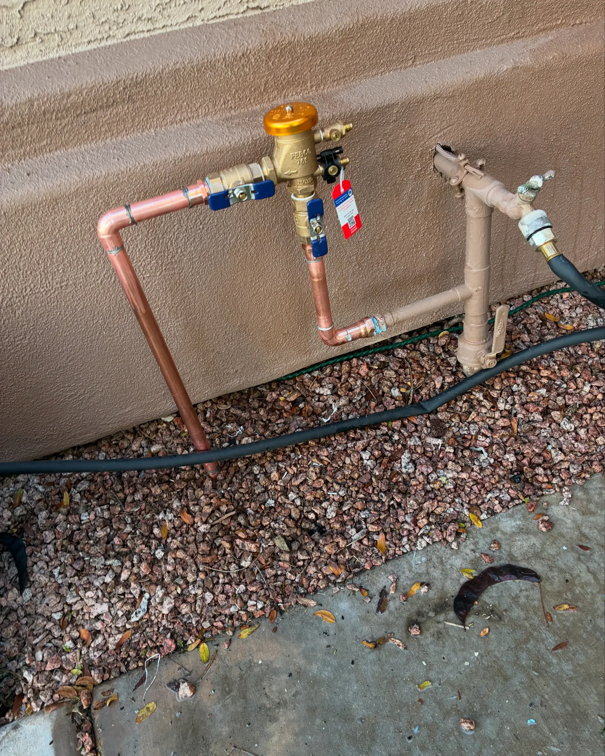 Copper and PVC water supply lines with brass valves and blue/red handles installed at foundation